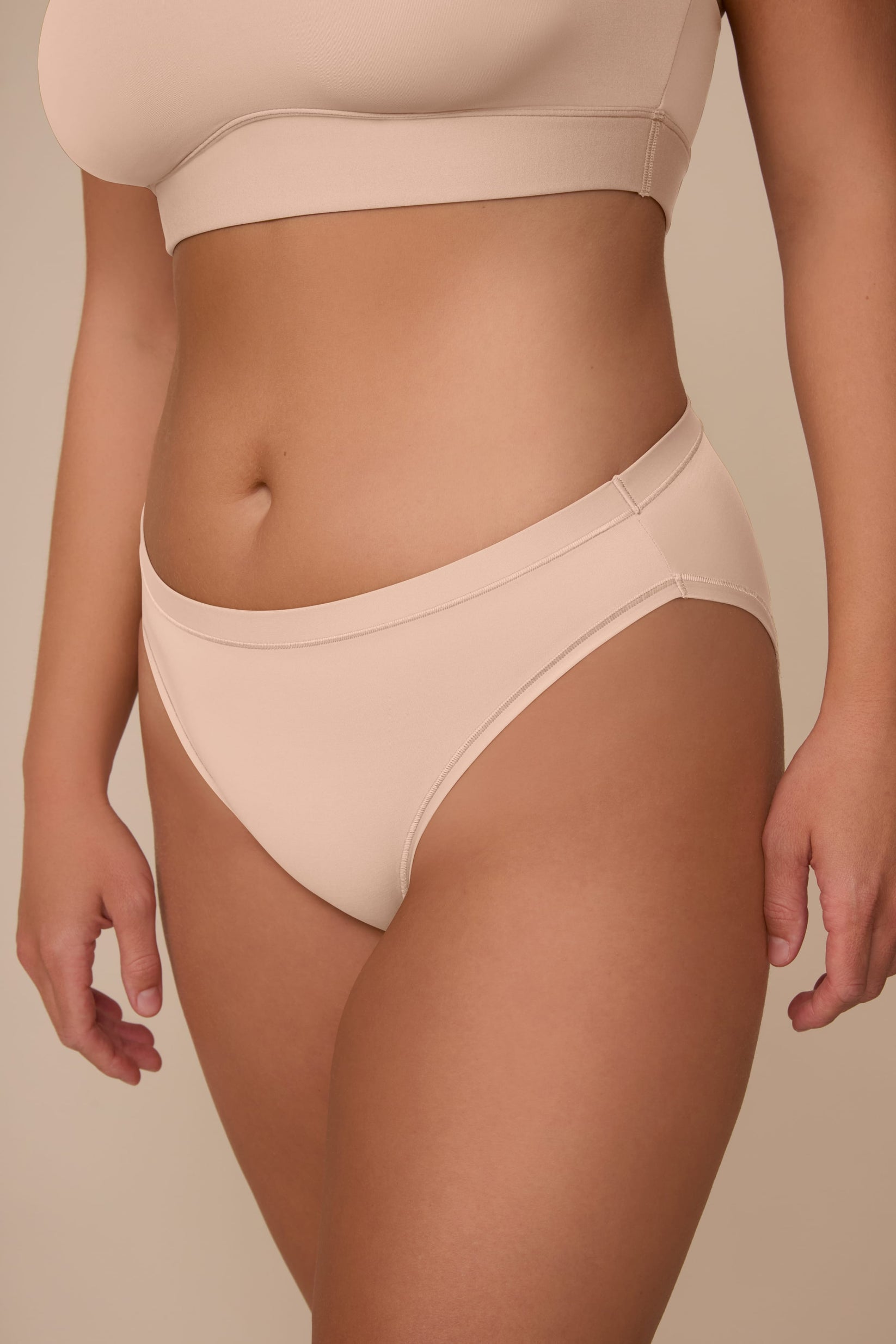 On a neutral beige backdrop, a close-up of the Bliss Bikini in Beige highlights the low-rise fit, smooth waistband, and soft fabric.