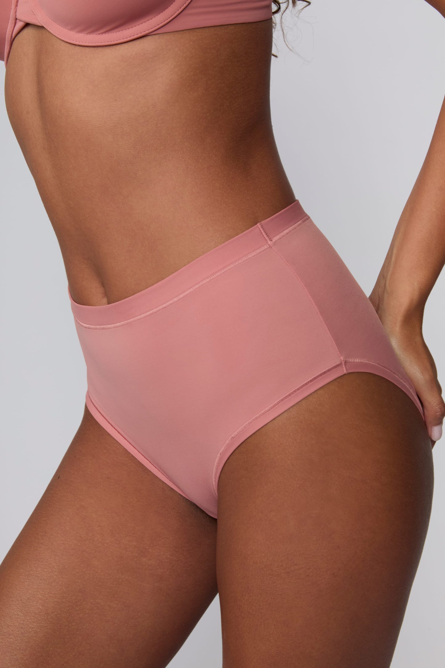 In a studio setting, Courtney wears the Bliss Highwaist Brief in Cinnamon. A side-angle close-up highlights the smooth fabric, high-rise waist, and full-coverage design.