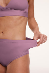 In a studio setting, Gianna wears the Bliss High Waist underwear in Mirage, shown in a close-up pulling the waistband to demonstrate stretch and flexibility. The fabric appears smooth and supportive.