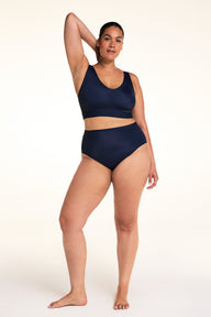 On a light studio backdrop, Jennifer wears the Bliss Highwaist in Navy with a matching navy bralette. The full-body image highlights the high-rise fit, smooth waistband, and full-coverage design.