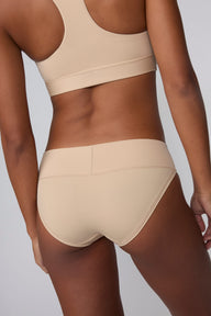 On a light gray studio backdrop, Amber wears the Bliss Low Rise Bikini in Beige with the matching Bliss Bralette in Beige. The back view highlights the full back coverage and smooth waistband.