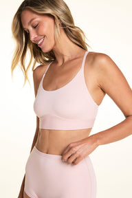 On a light studio backdrop, Meagan wears the Bliss Racerback Bralette in Ember Rose with matching bottoms. The angled view highlights the scoop neckline, adjustable straps, and wide comfort band.