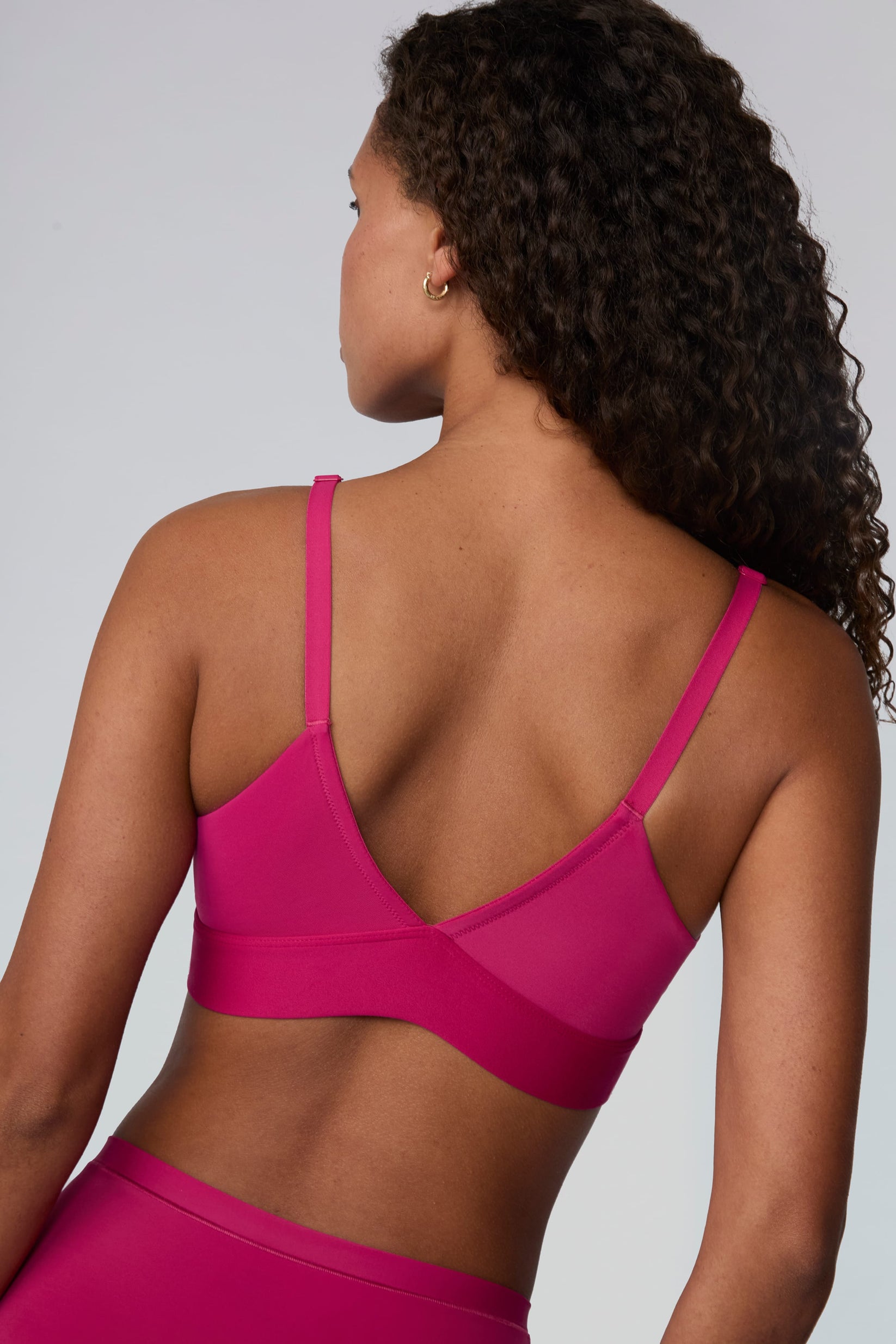 On a light gray studio backdrop, Courtney wears the Bliss Triangle Bralette in Winterberry. A back view highlights the V-shaped back design, adjustable straps, and smooth underband.