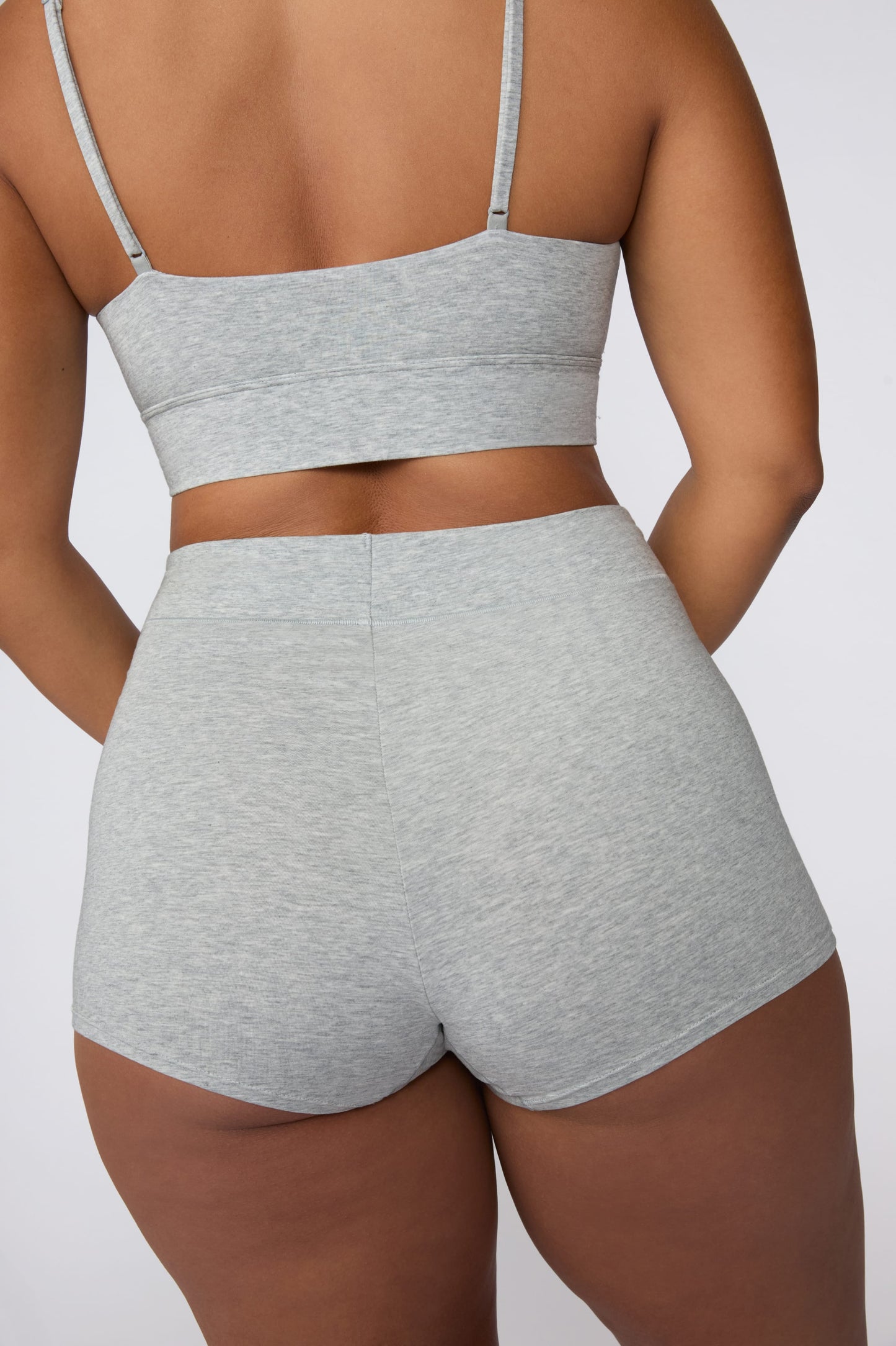 On a light gray studio backdrop, India wears the Cloud Cotton Boyshort in Heather Grey. The back view highlights the wide waistband, full back coverage, and soft cotton fabric.