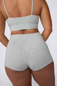 On a light gray studio backdrop, India wears the Cloud Cotton Boyshort in Heather Grey. The back view highlights the wide waistband, full back coverage, and soft cotton fabric.