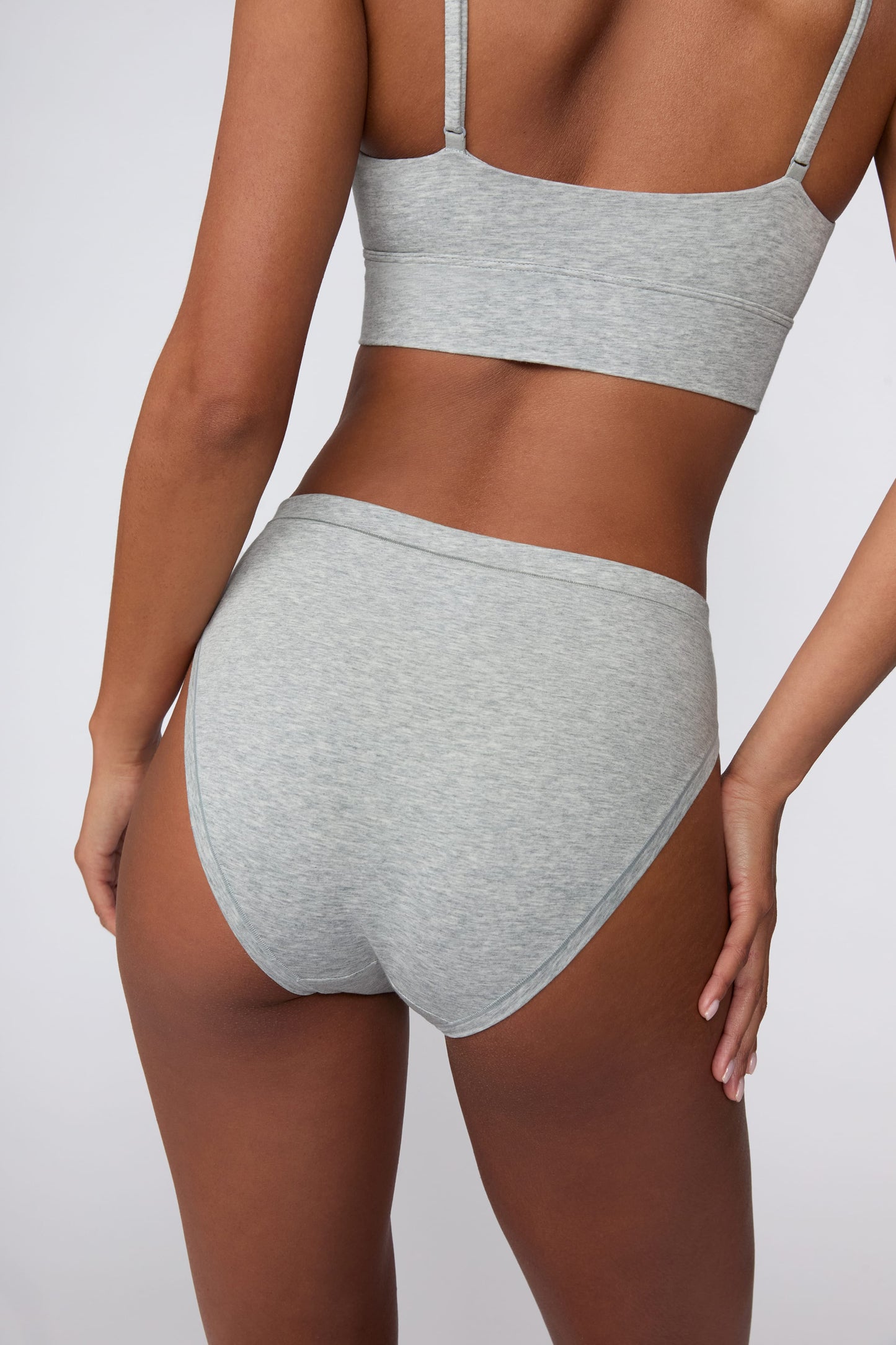 On a light gray studio backdrop, Courtney wears the Cloud Cotton French Cut Brief in Heather Grey. The back view highlights the full back coverage, smooth waistband, and soft cotton fabric.