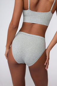 On a light gray studio backdrop, Courtney wears the Cloud Cotton French Cut Brief in Heather Grey. The back view highlights the full back coverage, smooth waistband, and soft cotton fabric.