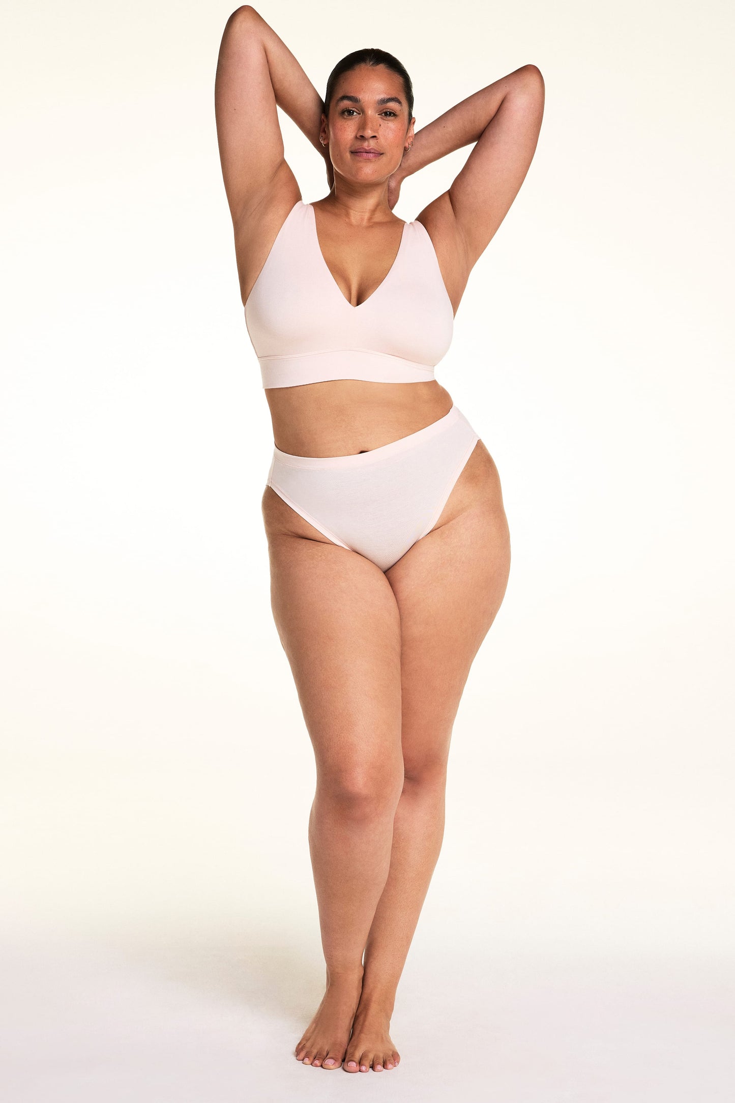 On a light studio backdrop, Jennifer wears the Cloud Cotton French Cut in Dogwood with the Bliss Triangle Bralette in Dogwood. The full-body image highlights the high-cut leg opening, smooth waistband, and comfortable cotton fit.