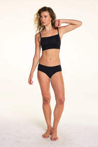 In a full-body studio portrait, Alexis wears the Cloud Cotton Hiphugger underwear in Black with a matching bralette, highlighting the low-rise fit and soft cotton fabric.