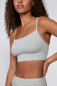 On a light gray studio backdrop, Courtney wears the Cloud Cotton Thin Strap Bralette in Heather Grey with matching underwear. The close-up view highlights the straight neckline, thin adjustable straps, and wide underband.