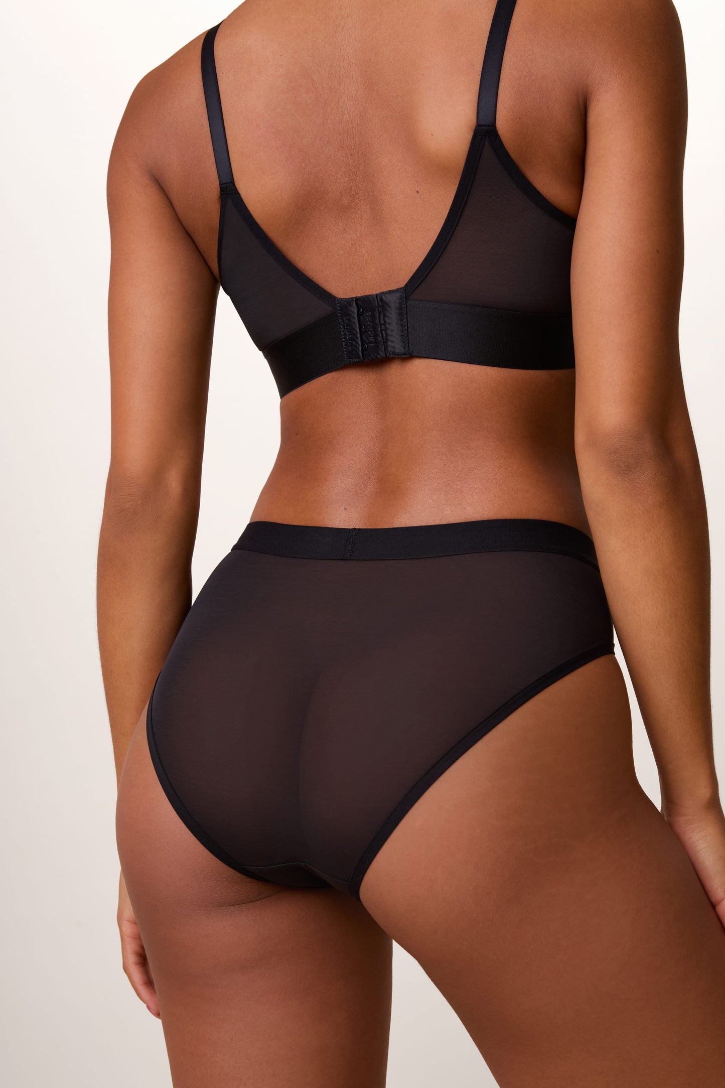 Back view of the ComfortMesh™ Highwaist Brief in Black on a light studio backdrop, showing the sheer mesh fabric and moderate back coverage.