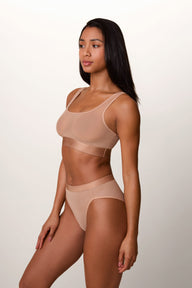 On a light studio backdrop, Ally wears the ComfortMesh™ Scoop Bralette in Taupe with the matching brief. A side-angle view highlights the scoop neckline, sheer mesh fabric, wide comfort band, and smooth fit.