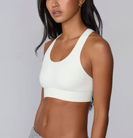 On a neutral studio backdrop, Amber is shown in a close-up front angle wearing the Seamless Racerback Sports Bra in White. The smooth scoop neckline, wireless support, and wide underband are visible.