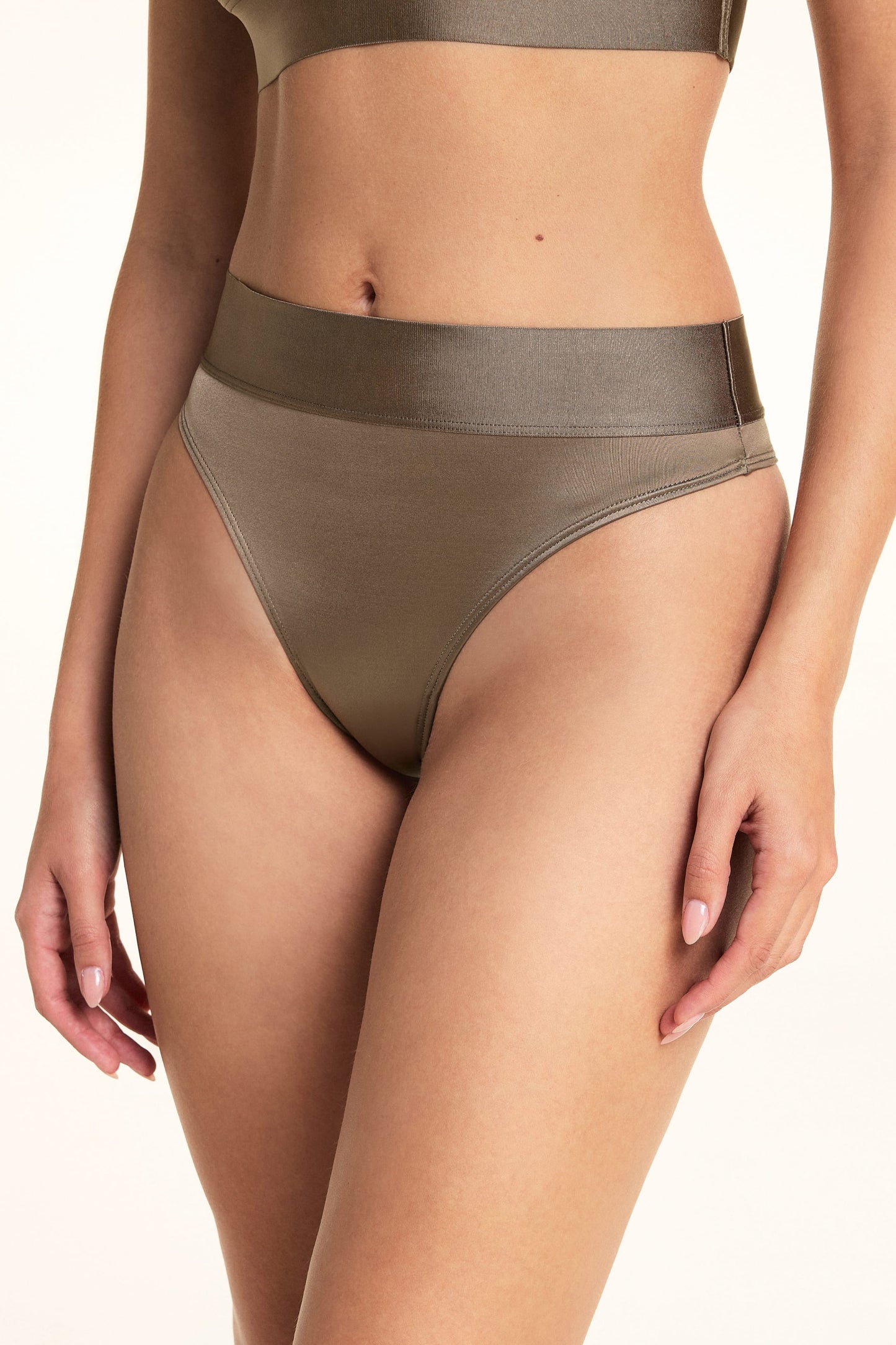 In a studio setting, Laura wears the Stretch Satin Square Neck Bralette and Stretch Satin Highwaist Thong in Sable, with a close-up view of the thong’s high waist, wide top band, and satin fabric.