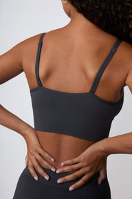 On a light gray studio backdrop, Courtney wears the Ribbed Seamless Triangle Bralette in Charcoal. A back view highlights the adjustable straps, ribbed texture, and wide underband.