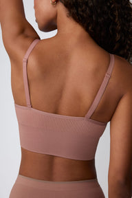 On a light gray studio backdrop, Courtney is shown from the back wearing the Ribbed Seamless Triangle Bralette in Plum. The close-up view highlights the adjustable straps, ribbed seamless fabric, and wide supportive band.