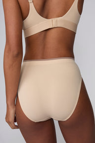 On a light gray studio backdrop, Courtney wears the Smooth Seamless Brief in Beige with the matching Smooth Seamless Bralette in Beige. The back view highlights the full back coverage, smooth finish, and contrast trim waistband.