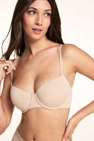 On a light neutral backdrop, Laura wears the Base Balconette Bra in Beige with matching underwear. The image highlights the balconette neckline, molded underwire cups, adjustable straps, and smooth finish.
