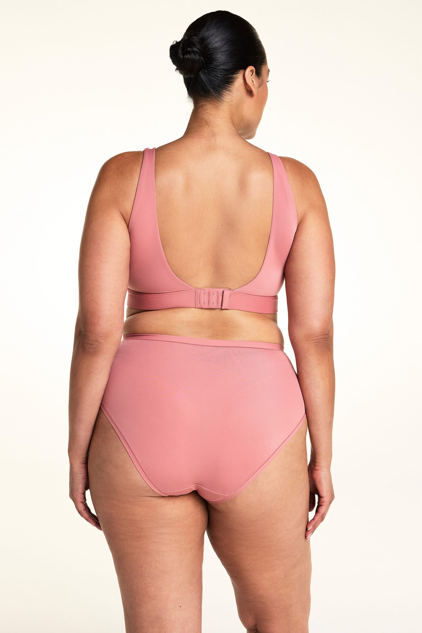 On a light neutral backdrop, Jennifer is shown from the back wearing the Bliss Scoop Adjustable Bralette in Cinnamon with matching underwear. The image highlights the scoop back, adjustable hook-and-eye closure, wide straps, and matching high-rise underwear.