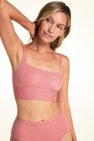 On a light neutral backdrop, Meagan wears the Bliss Squareneck Bralette in Cinnamon with matching underwear. She raises one arm to show the square neckline, thin straps, and longline wireless design.