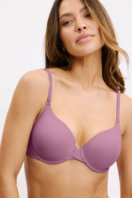 In a white studio setting, Darion wears the Base Bra in Mirage, featuring smooth molded cups, a scoop neckline, and adjustable straps.