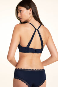 On a white studio backdrop, Laura wears the Base Lace T-Shirt Bra in Navy from the back, showing the cross-back strap configuration and lace back panel.