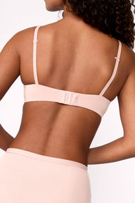 On a light studio backdrop, Courtney wears the Base T-Shirt Bra in Rose, shown from the back. The bra features adjustable straps and a hook-and-eye closure.