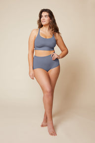 On a neutral beige backdrop, Summerlyn wears the Bliss Boyshort in Steel with a coordinating Bliss bralette, highlighting the high-rise silhouette and full-coverage fit in a full-body pose.