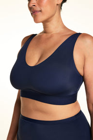 On a light studio backdrop, Jennifer wears the Bliss Bralette in Navy with matching underwear. The angled close-up highlights the V-neckline, wide wireless band, and ultra-soft microfiber fabric.