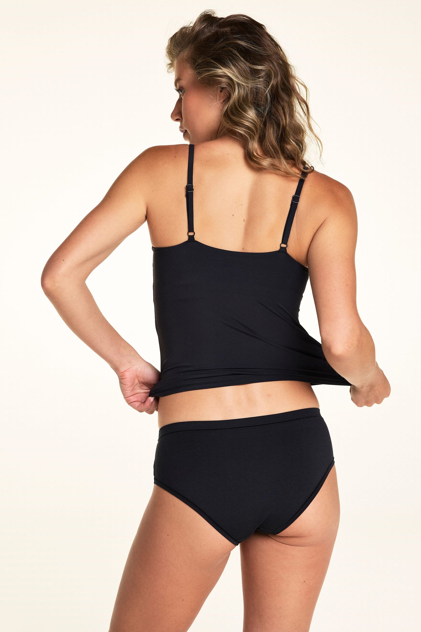 Seen from the back, Alexis wears the Bliss Cami in Black with matching underwear, showing the adjustable straps and smooth back design.