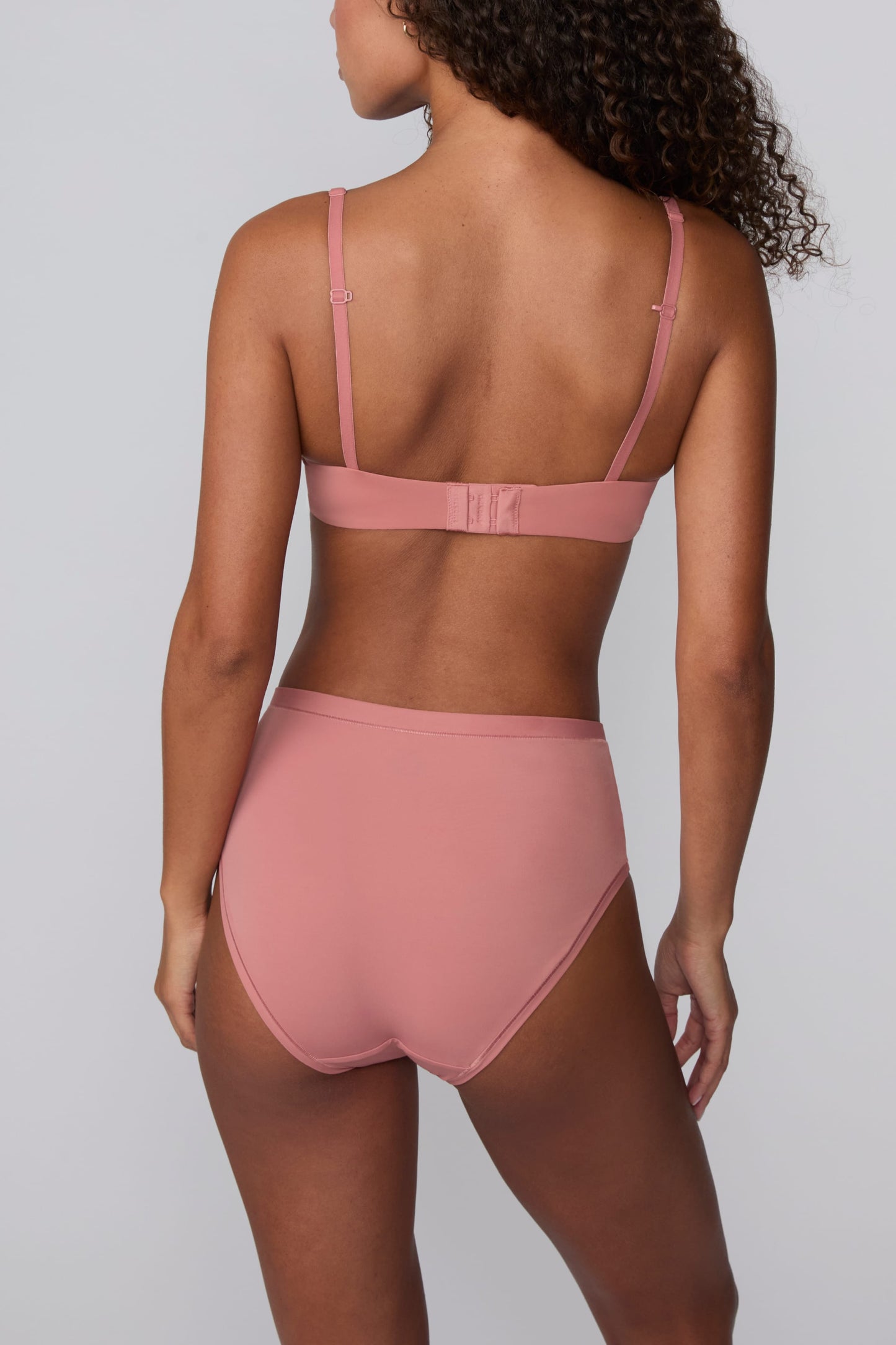 On a light gray studio backdrop, Courtney wears the Bliss Highwaist Brief in Cinnamon with a matching bra. A back view highlights the smooth fabric, high-rise waistband, and full back coverage.