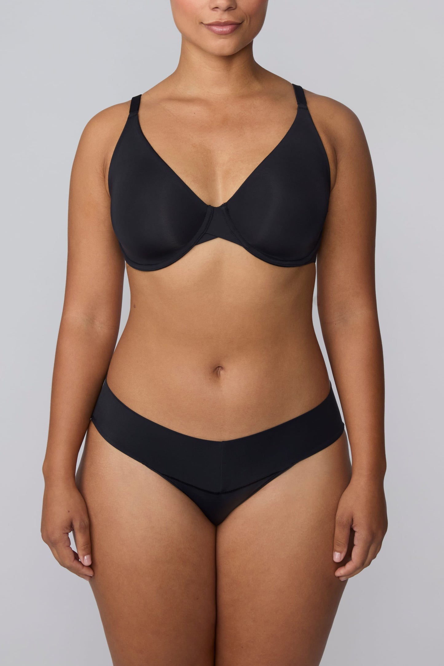 In a studio setting, India wears the Bliss Low Rise Bikini in Black with the matching bra in Black. The front view highlights the low-rise fit, smooth fabric, and clean waistband design.