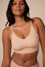 On a neutral studio backdrop, Victoria wears the Bliss Nursing Bralette in Beige with matching underwear. The close-up view highlights the scoop neckline, nursing clips, smooth fabric, and wireless design.