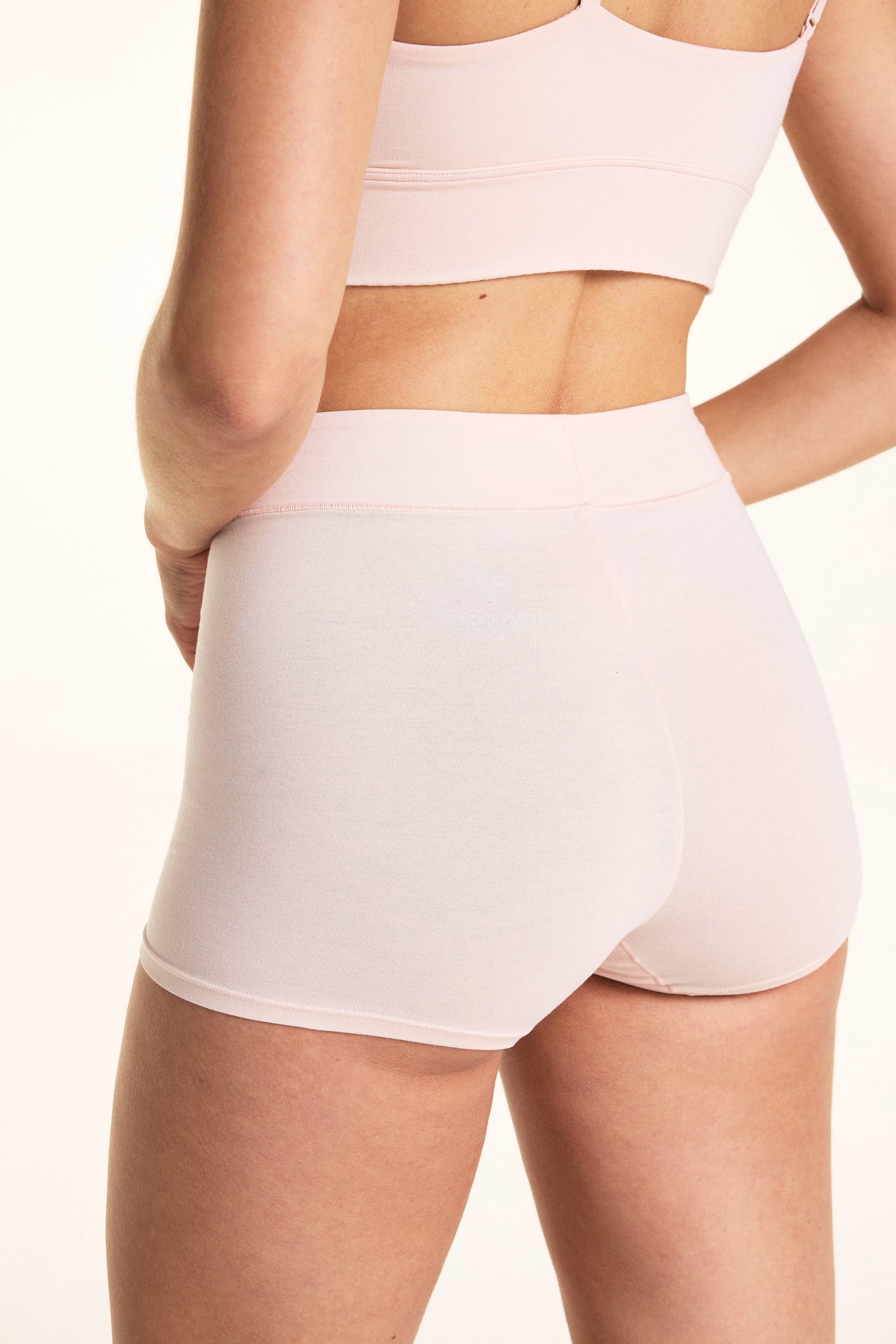 On a light studio backdrop, Laura wears the Cloud Cotton Highwaist Boyshort in Dogwood with the Bliss Triangle Bralette in Dogwood. The back view highlights the high-rise waistband, full-coverage back coverage, and smooth cotton fabric.