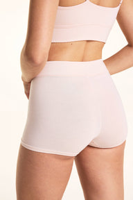 On a light studio backdrop, Laura wears the Cloud Cotton Highwaist Boyshort in Dogwood with the Bliss Triangle Bralette in Dogwood. The back view highlights the high-rise waistband, full-coverage back coverage, and smooth cotton fabric.