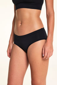 From a side angle in the studio, Alexis wears the Cloud Cotton Hiphugger underwear in Black, showing the smooth waistband and hiphugger silhouette.