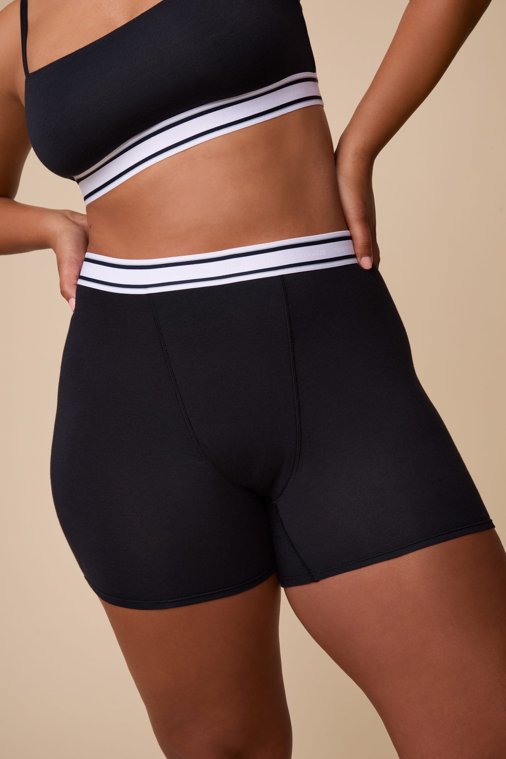 On a neutral studio backdrop, India wears the Cloud Cotton Retro Boxer Brief in Black. The close-up front view highlights the full-coverage boxer brief silhouette, smooth cotton modal fabric, and retro-inspired logo waistband.