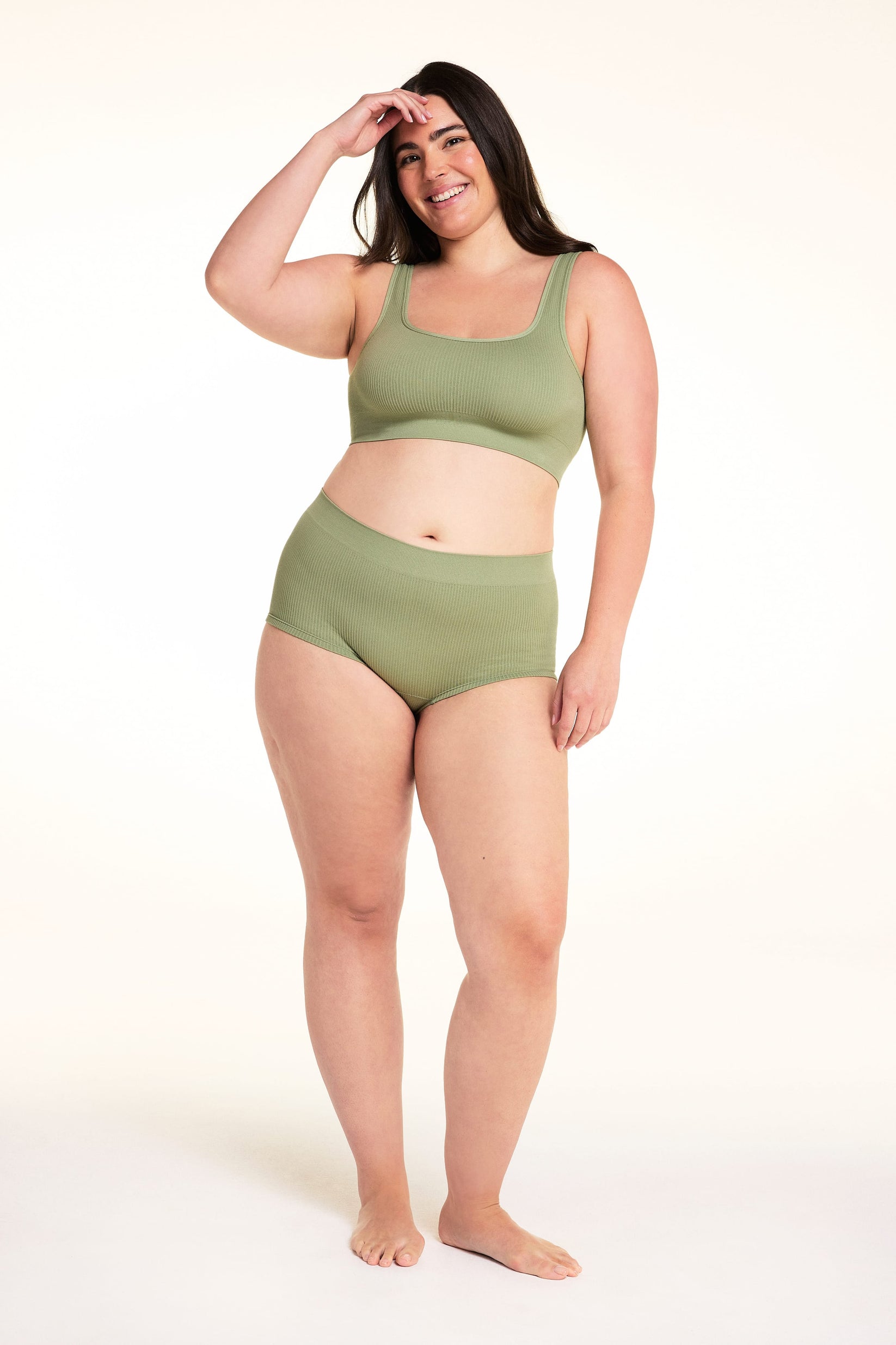 On a white studio backdrop, Alessandra wears the Lounge Rib Sleepshort in Dill with the matching Lounge Rib bralette, showing the ribbed fabric, scoop neckline, and short silhouette. sizing: Alessandra wears Large
