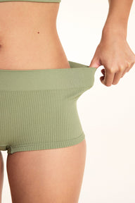 On a white studio backdrop, a close-up of Laura wearing the Lounge Rib Sleepshort in Dill shows the ribbed fabric as she gently stretches the waistband to demonstrate its flexibility.