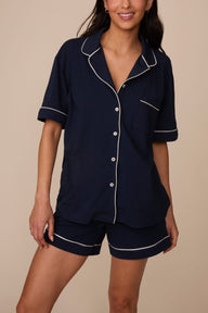 On a neutral studio backdrop, Marcela wears the Perfect Pima Pajama Short in Navy with the matching Perfect Pima Pajama Shirt in Navy. The front view showcases the relaxed fit, elastic waistband, side pockets, and contrast piping details throughout the set.