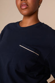 On a warm beige studio backdrop, Zarria wears the Perfect Pima Pajama T-Shirt in a deep navy color. The close-up detail view highlights the crew neckline and chest pocket finished with contrasting piping.