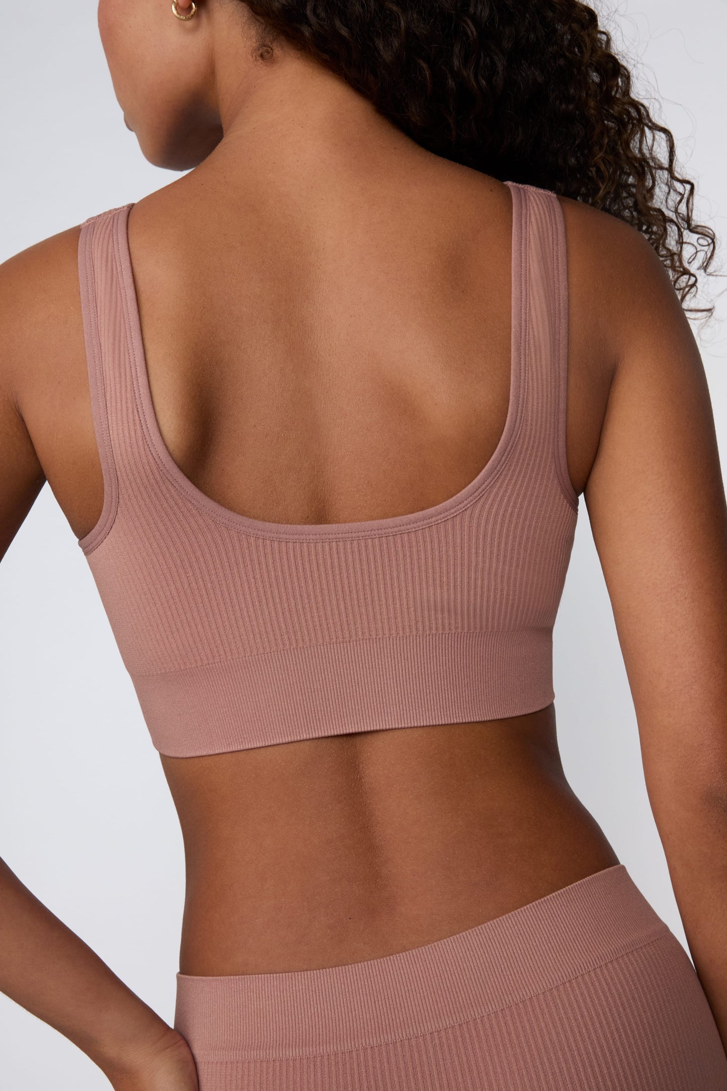 In a studio setting, Courtney wears the Ribbed Seamless Scoop Bralette in Plum. A back view highlights the scoop back, wide straps, supportive underband, and ribbed texture.