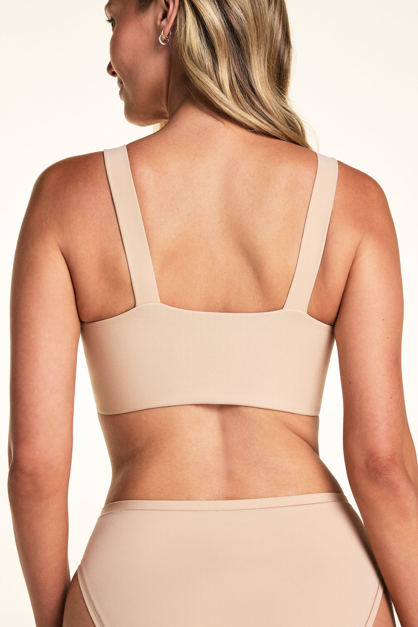 On a light neutral backdrop, Meagan is shown from the back wearing the Bliss Smoothing Bralette in Beige with matching underwear. The image highlights the straight back, wide straps, and smooth band.