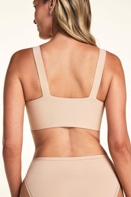 On a light neutral backdrop, Meagan is shown from the back wearing the Bliss Smoothing Bralette in Beige with matching underwear. The image highlights the straight back, wide straps, and smooth band.