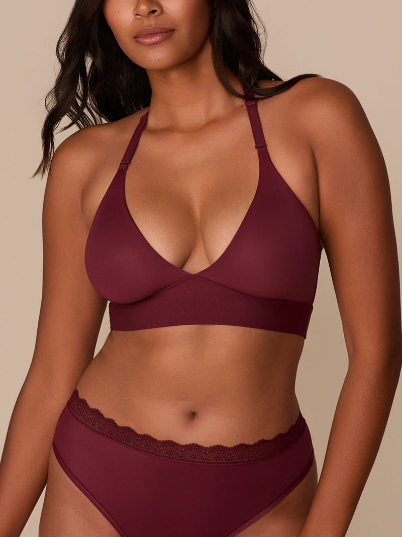 Close-up of a model wearing the Bliss Lace Halterneck Bralette in Bordeaux. The image highlights the deep V neckline and adjustable halter straps of the wireless bralette. The matching Bliss Lace Highwaist Brief is partially visible, showing the soft lace trim along the waistband.