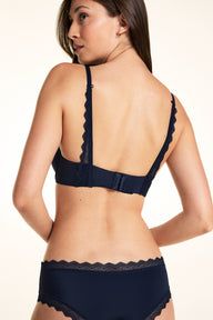 On a white studio backdrop, Laura wears the Base Lace T-Shirt Bra in Navy from the back, showing the adjustable straight straps and back hook-and-eye closure.