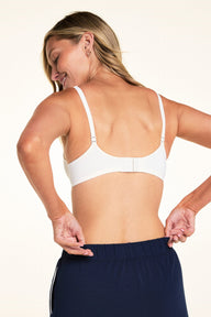On a light studio backdrop, Meagan is shown from the back wearing the Base Picot T-Shirt Bra in Ivory with the straps in the standard configuration. The image highlights the adjustable straps and back hook-and-eye closure.