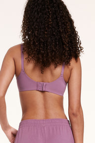 In a studio setting, Courtney wears the Base Unlined Bra in Mirage, shown from the back with adjustable straps and a hook-and-eye closure. The smooth microfiber band sits comfortably across the back.