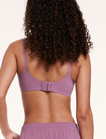 In a studio setting, Courtney wears the Base Unlined Bra in Mirage, shown from the back with adjustable straps and a hook-and-eye closure. The smooth microfiber band sits comfortably across the back.