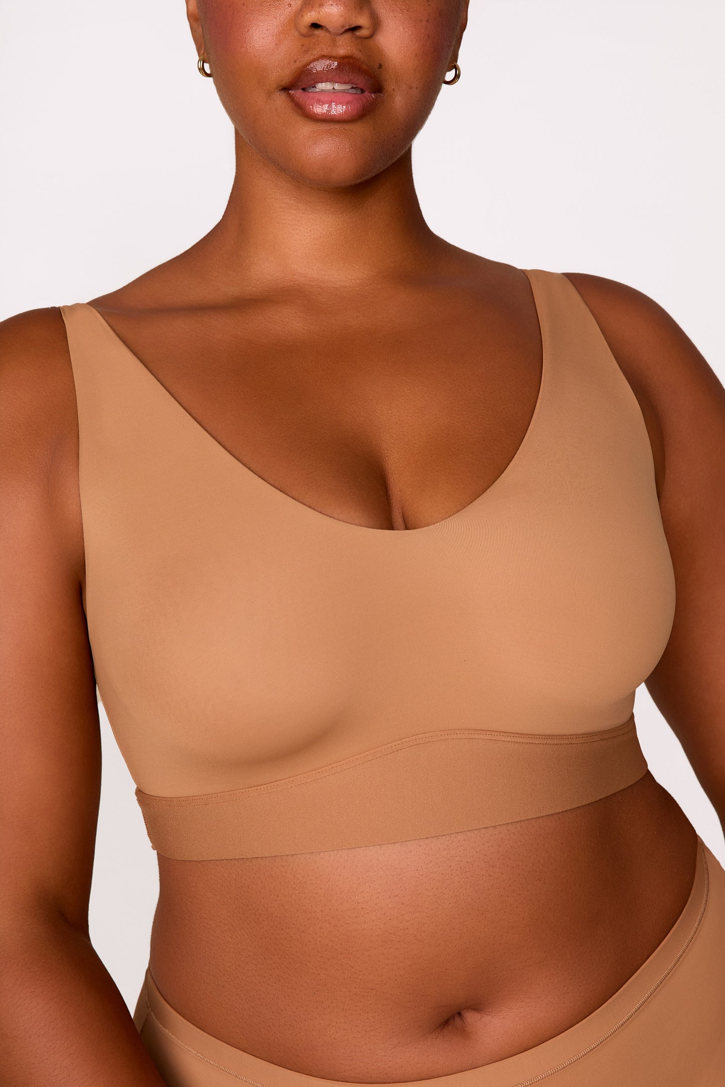 On a white studio backdrop, Zarria wears the Bliss Bralette in Tan, showing the V-neckline, wide straps, and smooth fabric from the front. sizing: Zarria wears size XL
